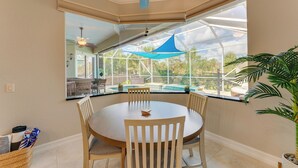 Un coin repas comprenant une table ronde, quatre chaises, un ventilateur de plafond et une grande fenêtre donnant sur un paysage verdoyant.