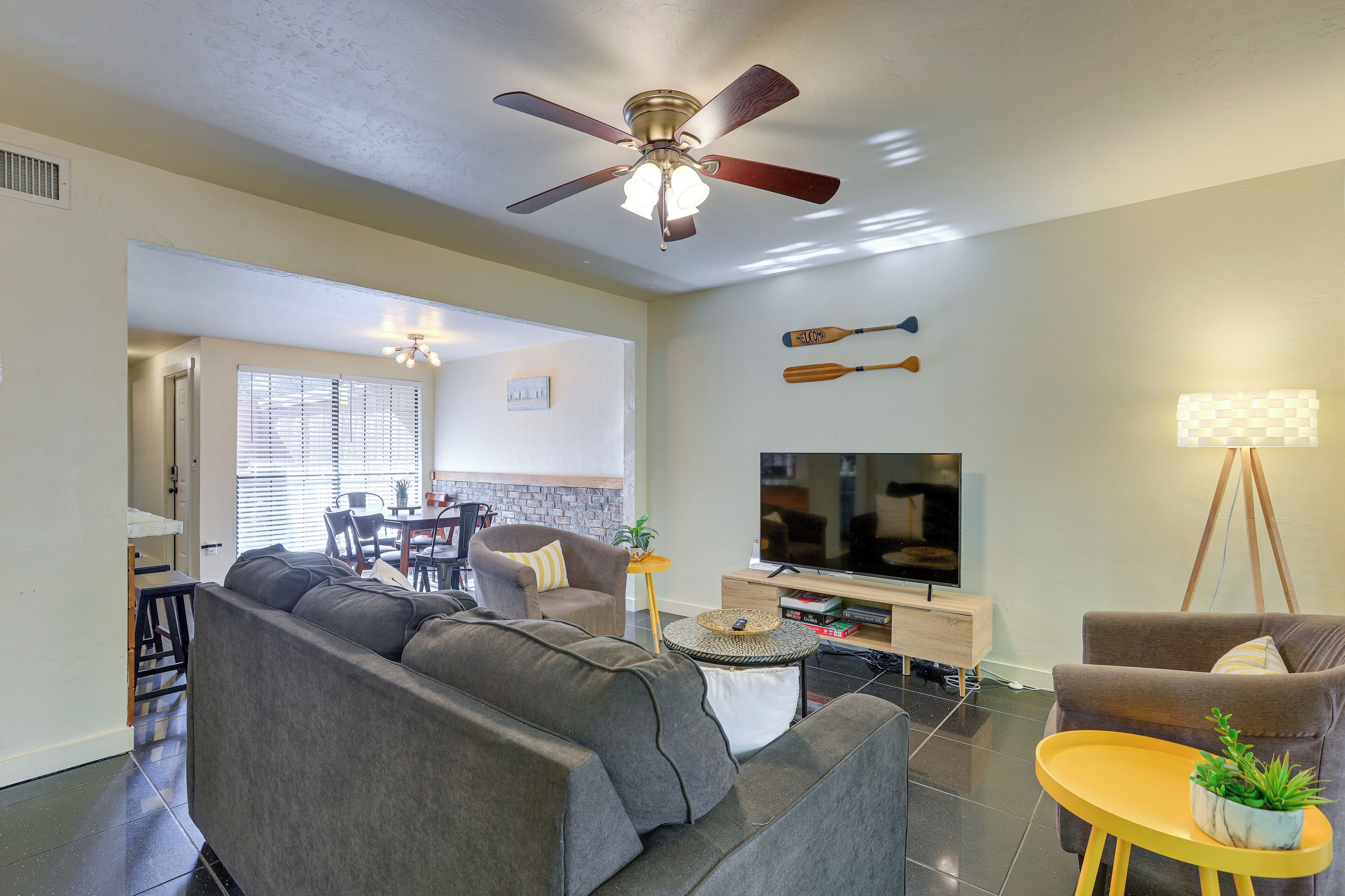 A modern living room with a grey sectional sofa, a small round table with a plant, a ceiling fan, and a flat-screen TV.