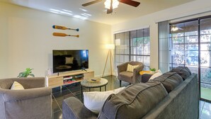Una sala de estar con ventilador de techo, televisor de pantalla plana, sofá, mesa de centro y ventana con persianas.