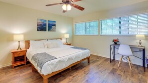 Un dormitorio con una cama de madera, dos mesitas de noche con lámparas, un escritorio con silla e un ventilador de techo.
