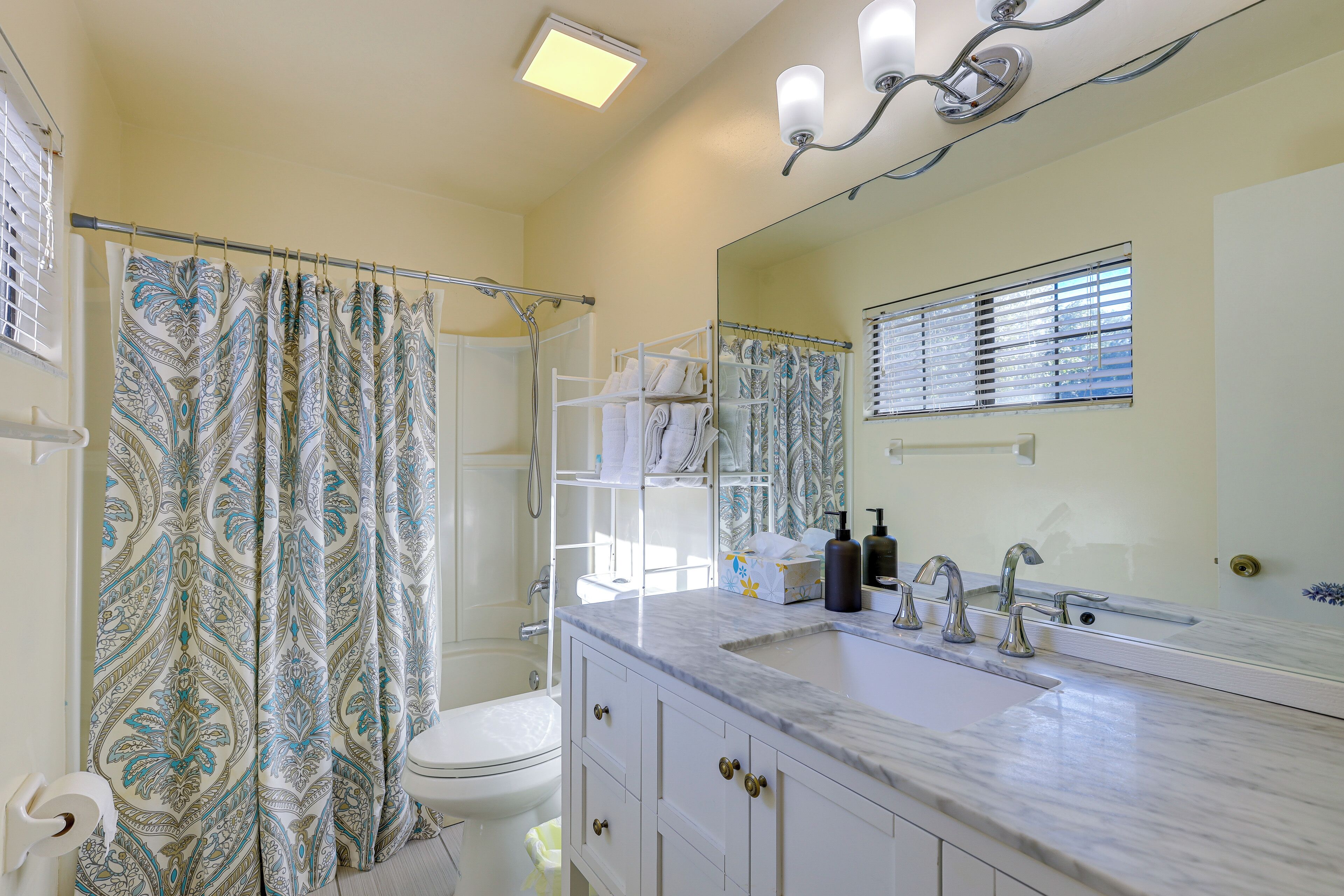 A bathroom with a shower curtain, a toilet, a sink with a mirror, and a towel rack.
