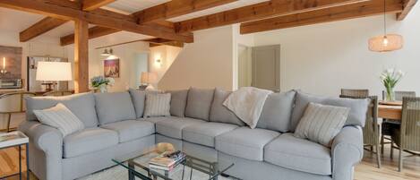 A modern living room with a grey sectional sofa, a glass coffee table, and wooden beams on the ceiling.