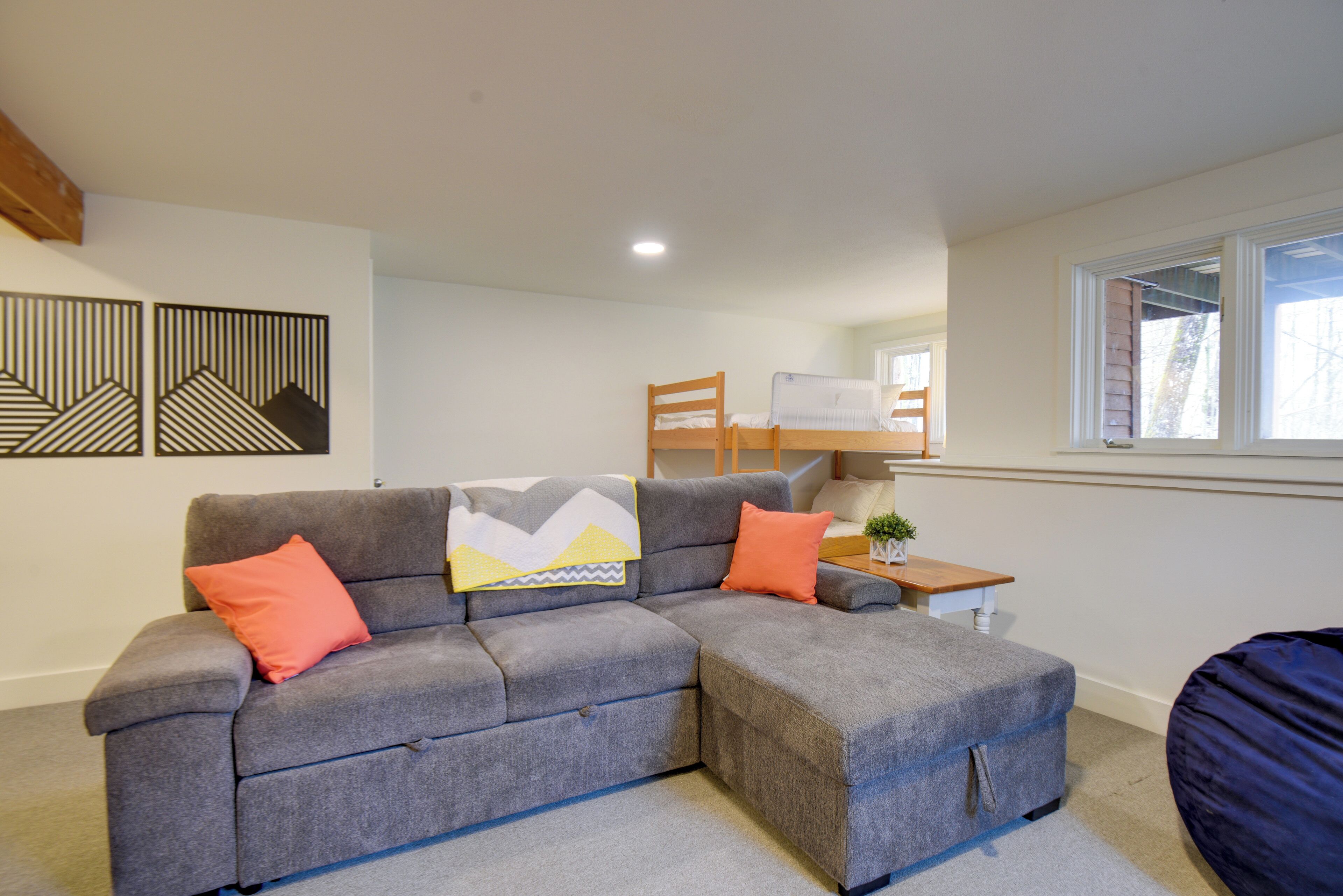 A modern living room with a grey sectional sofa, a wooden chair, a small table with a plant, and a window with a view.