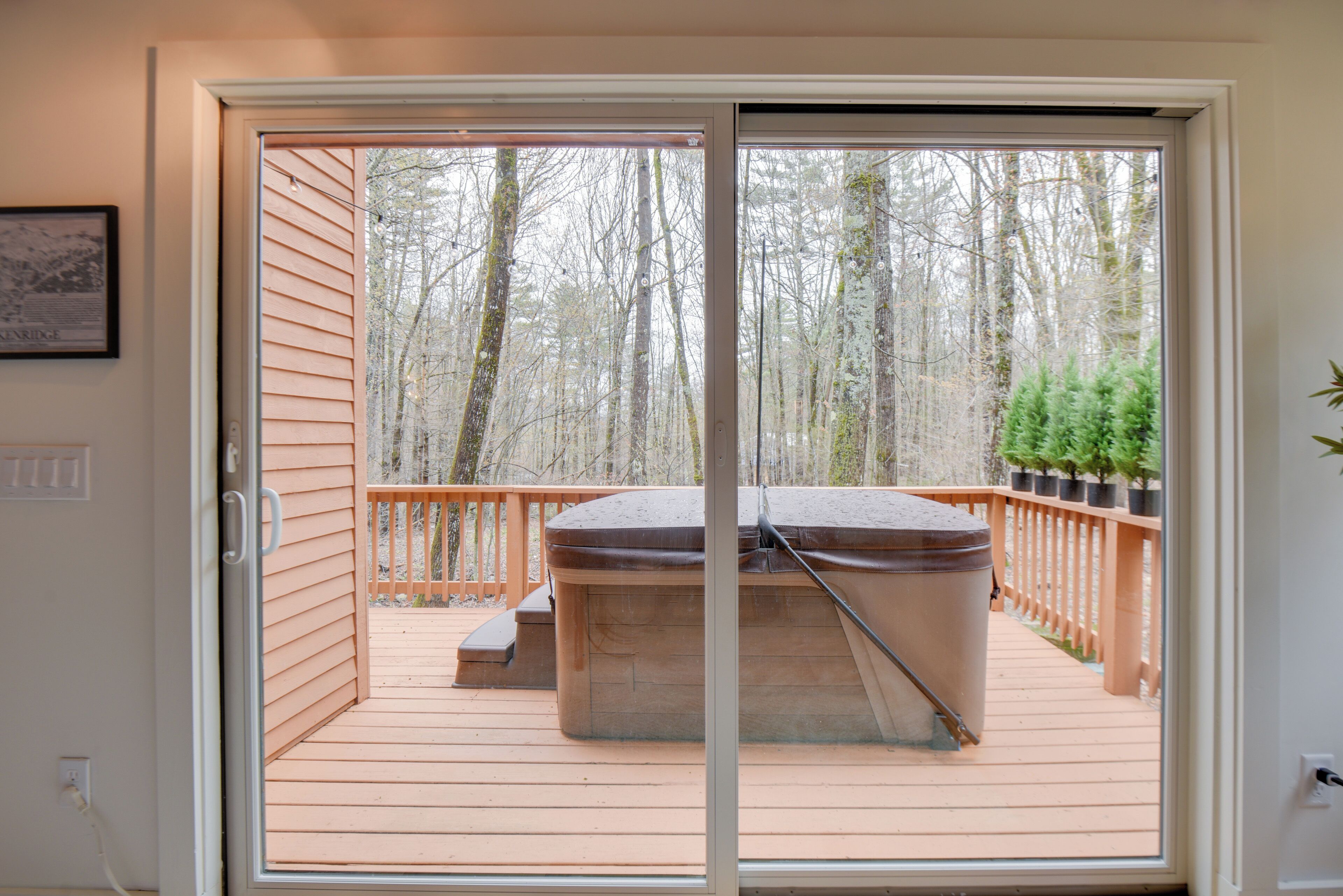 A deck with a hot tub, wooden railings, and a view of a forest.