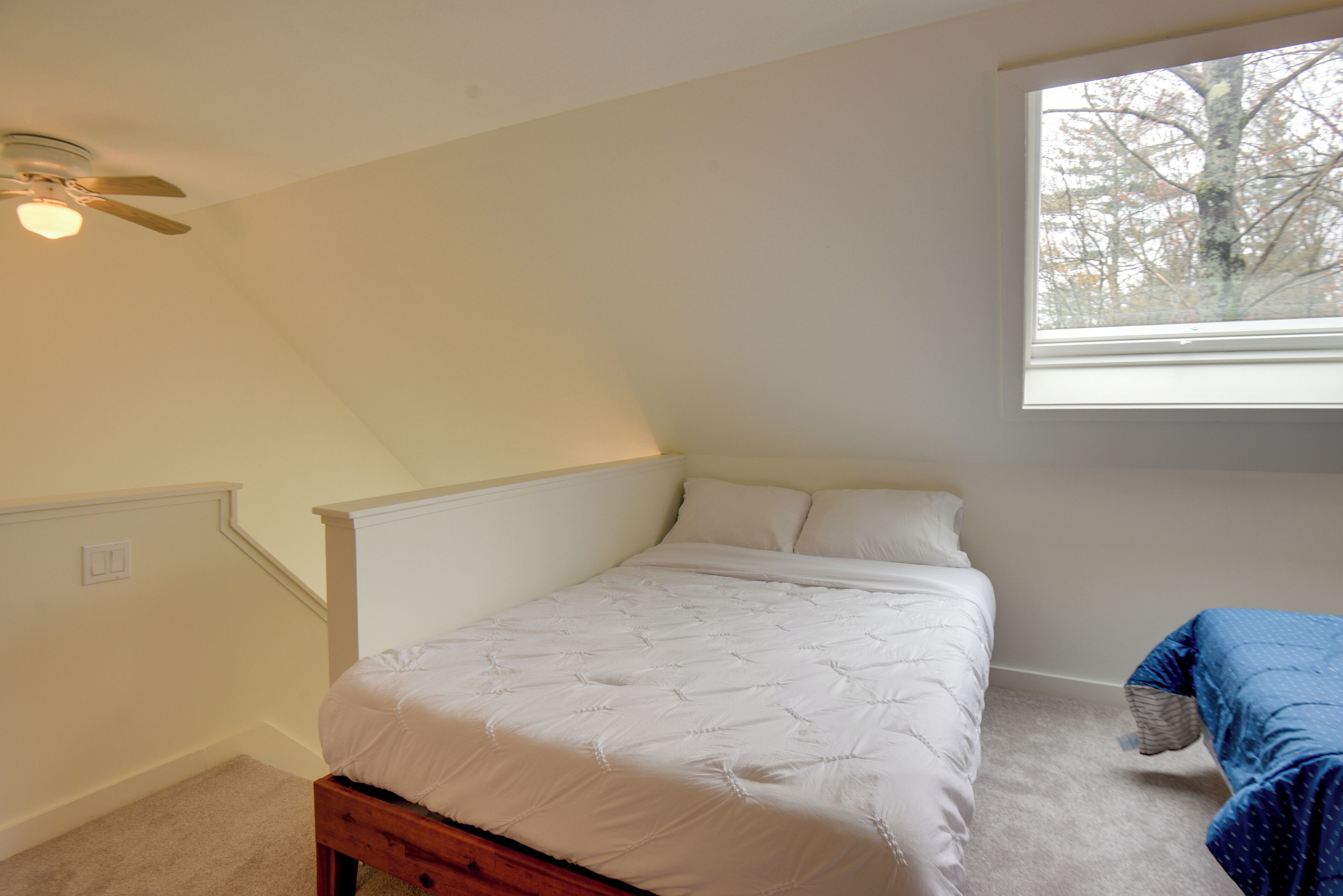 Ein Schlafzimmer mit einem Bett, einem Fenster, einem Deckenventilator und Teppichboden.