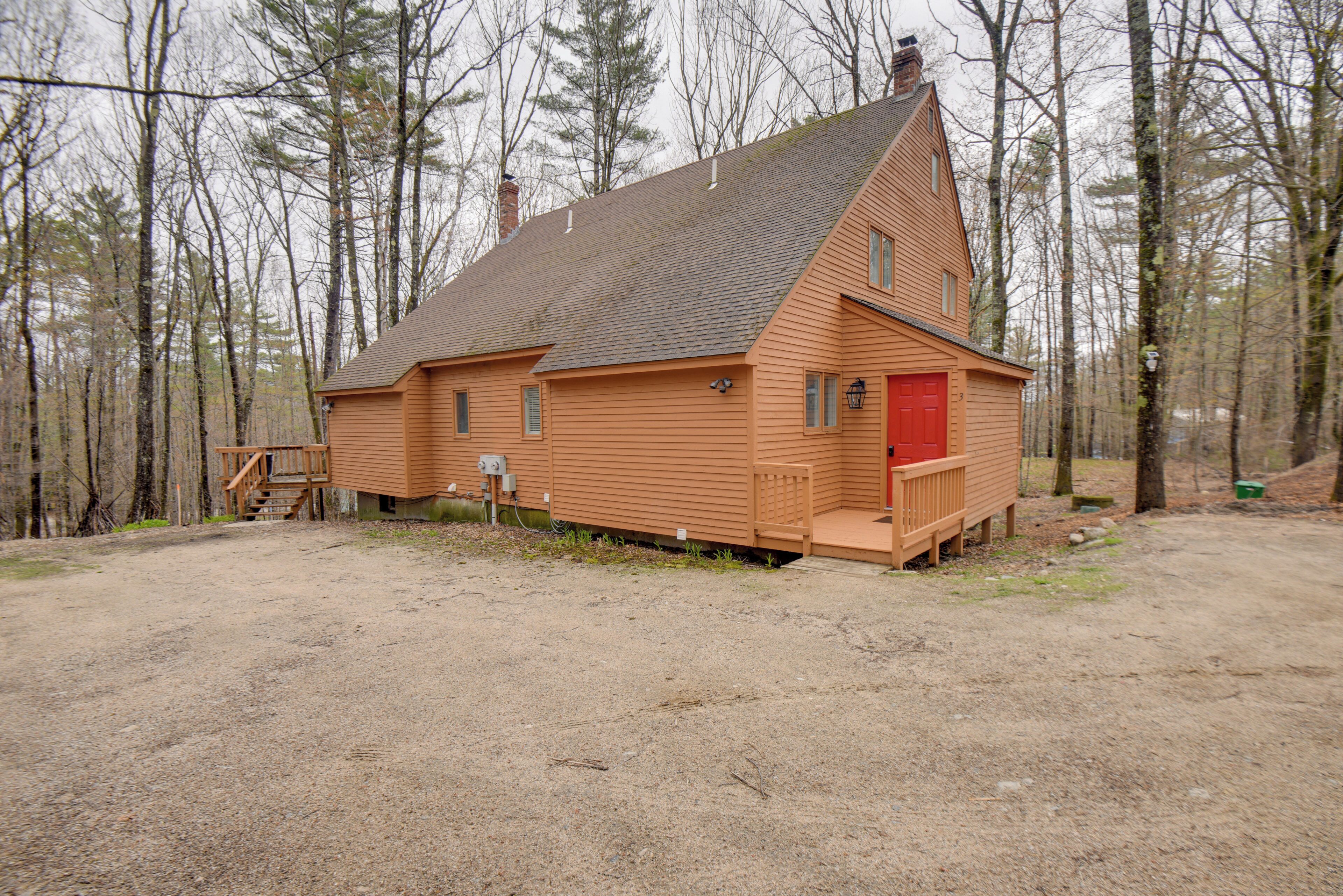 A wooden cabin with a red door, a small porch, and a chimney.