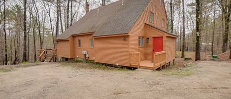 A wooden cabin with a red door, a small porch, and a chimney.