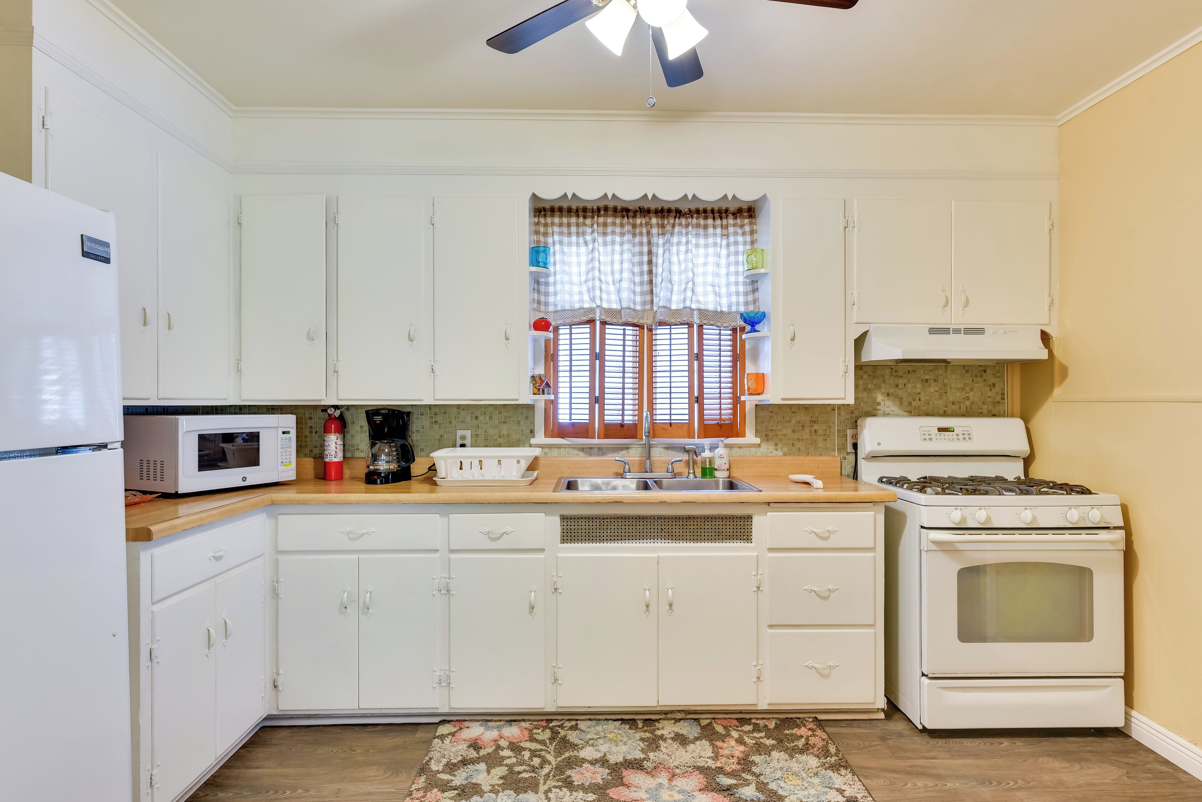 A kitchen with white cabinets, a microwave, a stove, and a window with curtains.