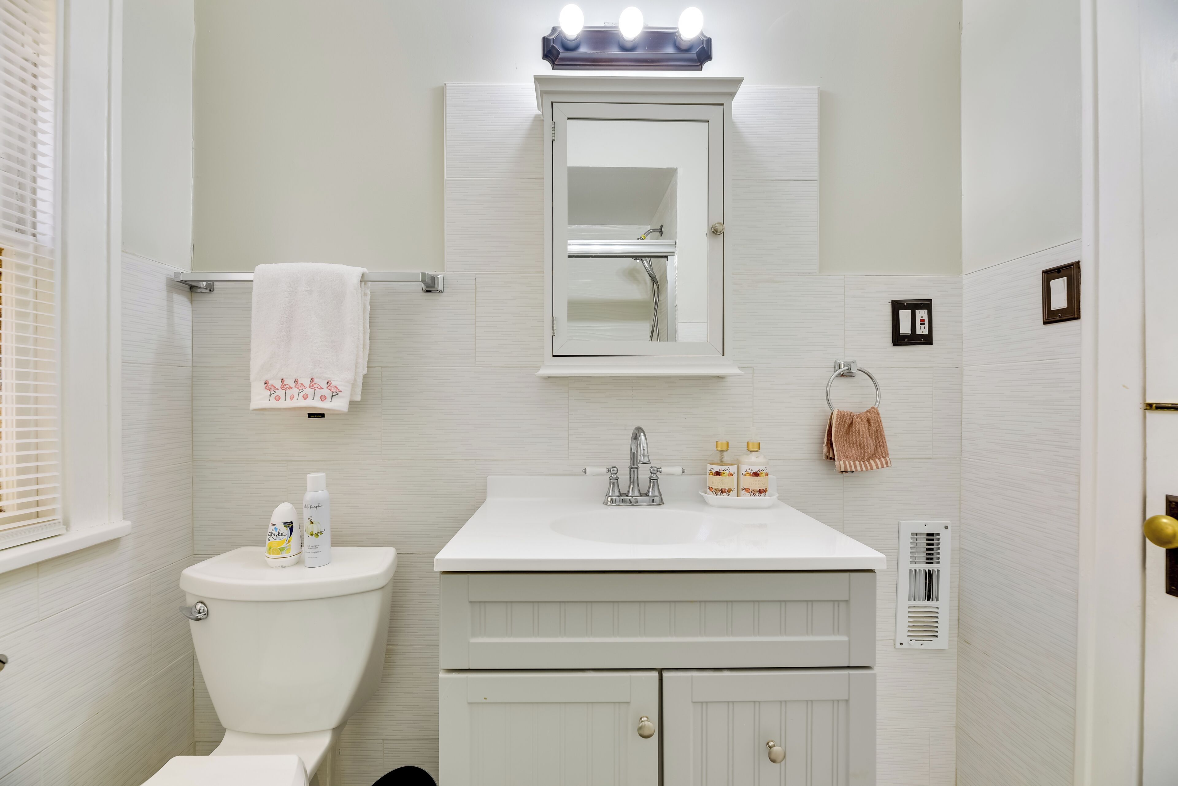 Une salle de bain avec des toilettes blanches, un lavabo surmonté d’un miroir et une serviette suspendue à un porte-serviettes.