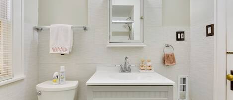 Une salle de bain avec des toilettes blanches, un lavabo surmonté d’un miroir et une serviette suspendue à un porte-serviettes.