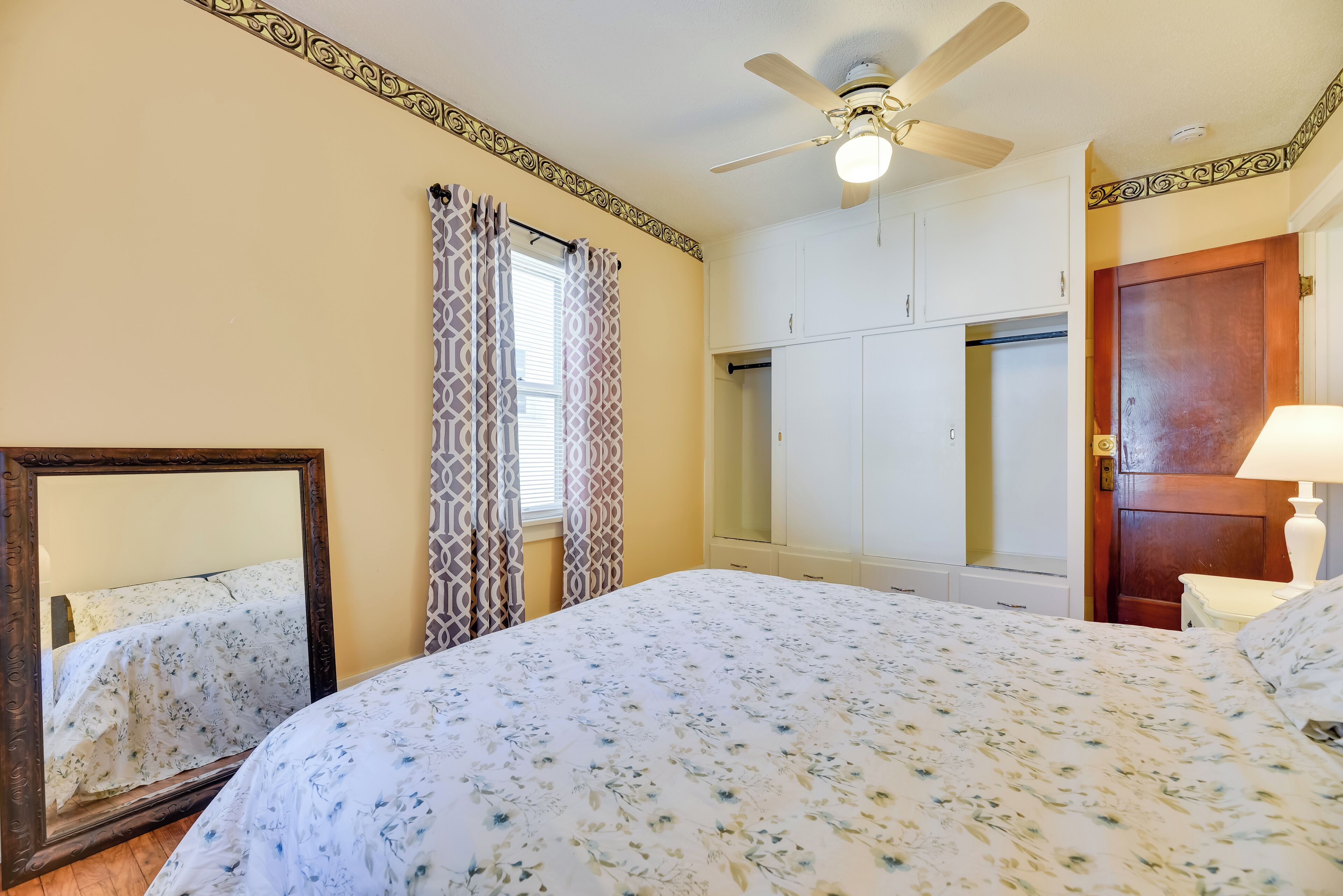 A bedroom with a bed, a wardrobe, a ceiling fan, and a mirror.