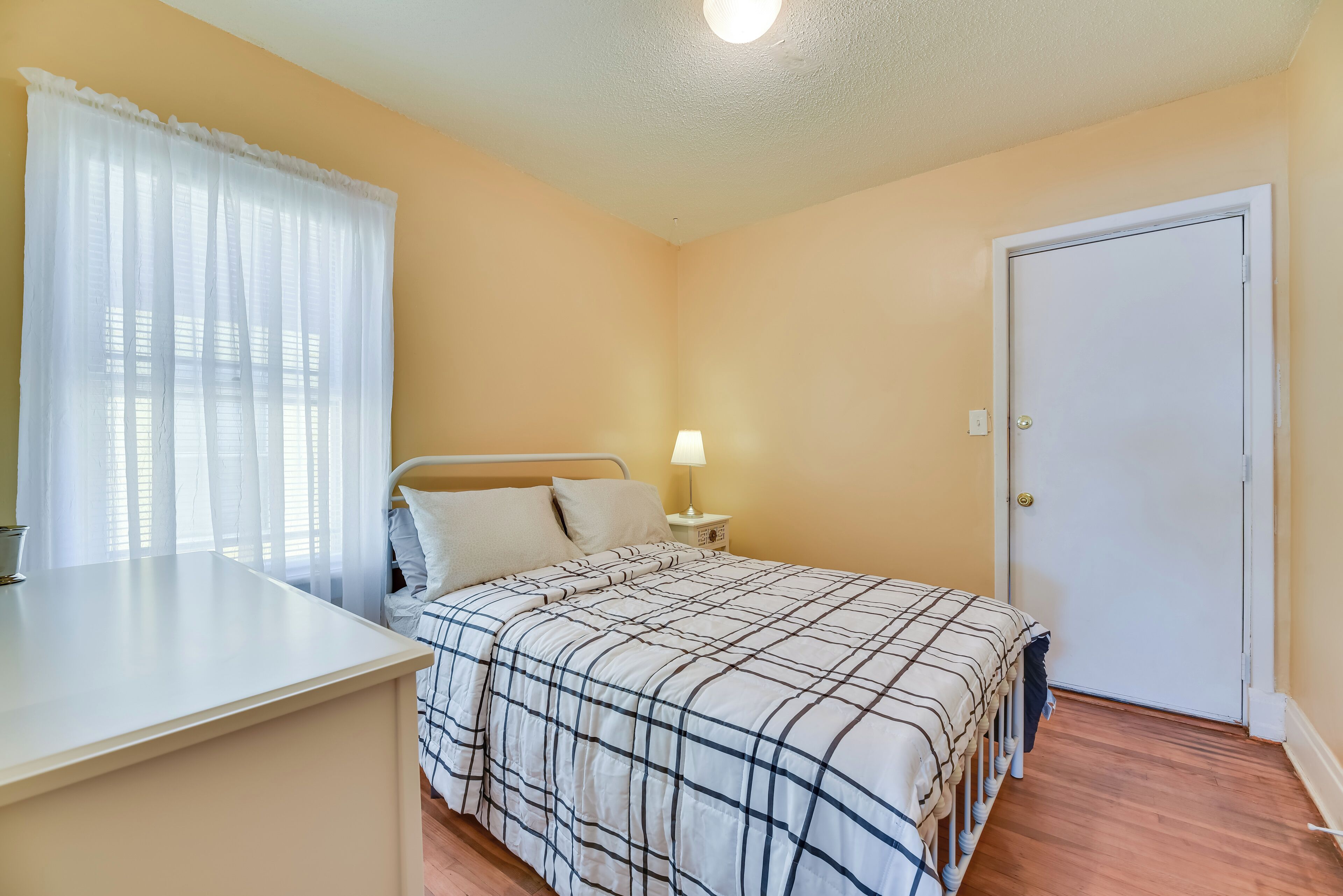A bedroom with a bed, a bedside table, a lamp, and a door.