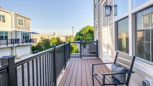 Une terrasse en bois avec une rambarde noire, un banc et un pot de fleurs.