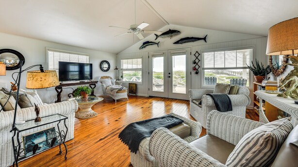 A spacious living room with wicker furniture, a ceiling fan, and a large window with a view. - Oceanfront Amelia Island Cottage: Deck & Boardwalk (Fernandina Beach)