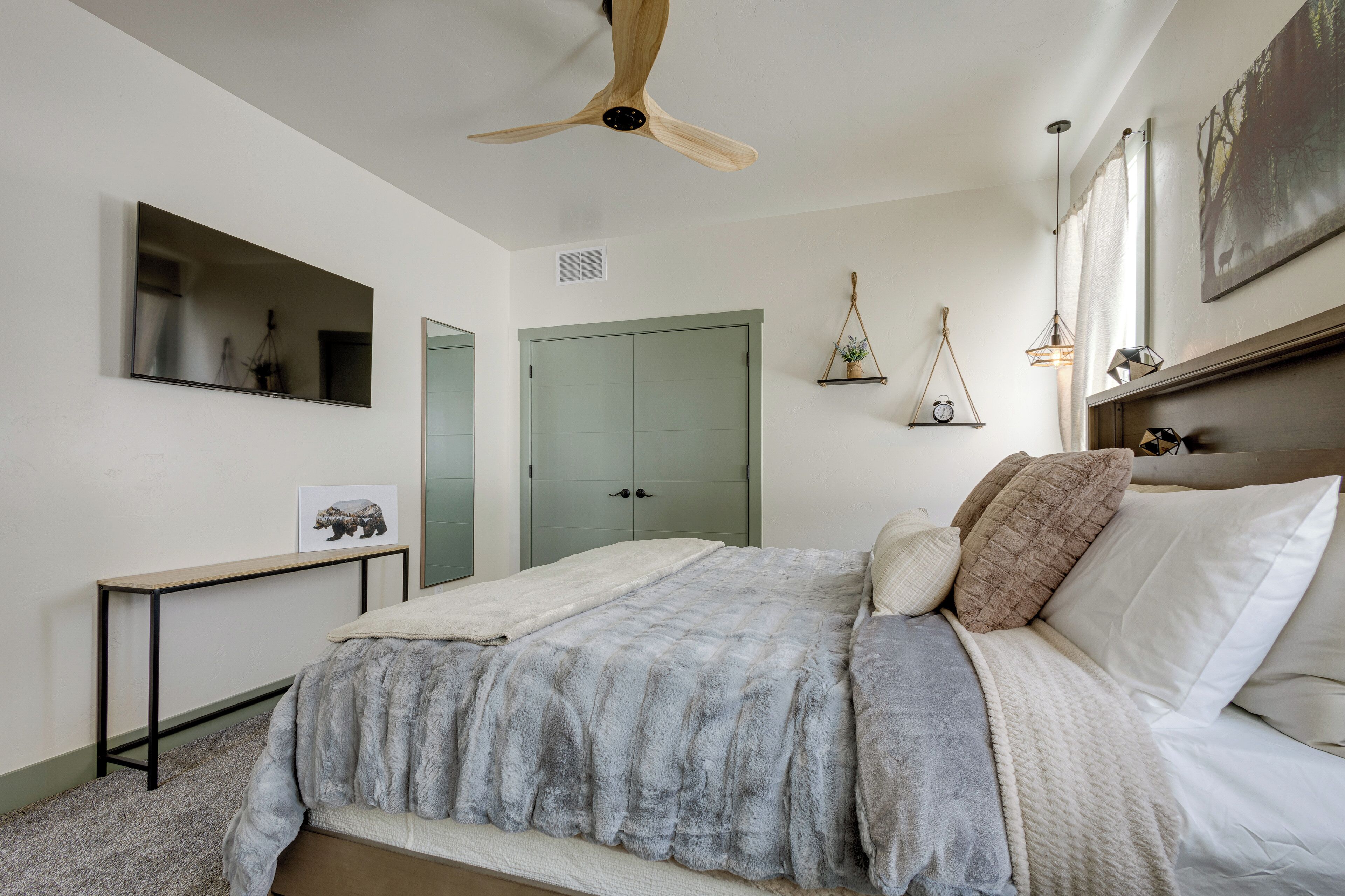 A bedroom with a bed, a ceiling fan, a bedside table, a mirror, and a door.