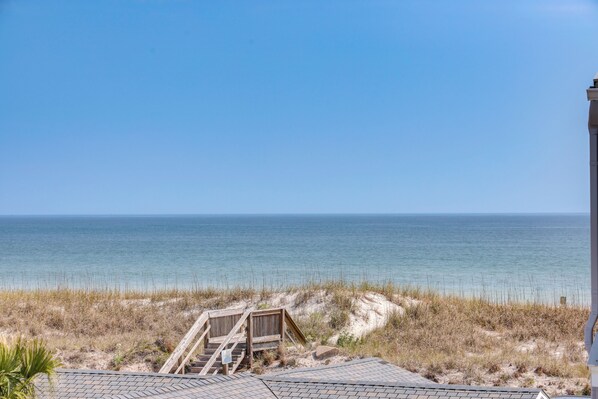 A beach view with a wooden staircase leading to a sandy area, a clear sky, and the ocean in the background.