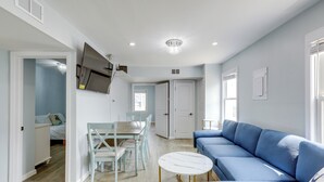 A modern living room with a blue sofa, a round white table, and a dining area with a table and chairs.