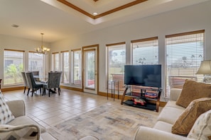 A spacious living room with a dining area, large windows, a chandelier, and a flat-screen TV. - Swim, Golf & Unwind: Laguna Vista Vacation Home! (Port Isabel)