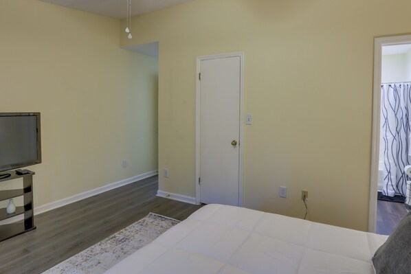 A bedroom with a bed, a television on a stand, a door, and a light switch on the wall. - 4 Mi to Dtwn: Pet-friendly Abode in Tallahassee! (Tallahassee)