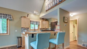 A kitchen with wooden cabinets, a stainless steel refrigerator, and a bar area with two blue chairs. - Lakefront Cabin on Secord Lake Sleeps 6 (Alger)