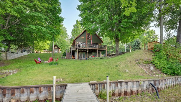 A wooden deck leading to a house with a balcony, surrounded by a grassy yard and trees. - Lakefront Cabin on Secord Lake Sleeps 6 (Alger)
