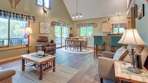 A spacious living area with a dining table, comfortable seating, and a kitchen in the background. - Lakefront Cabin on Secord Lake Sleeps 6 (Alger)