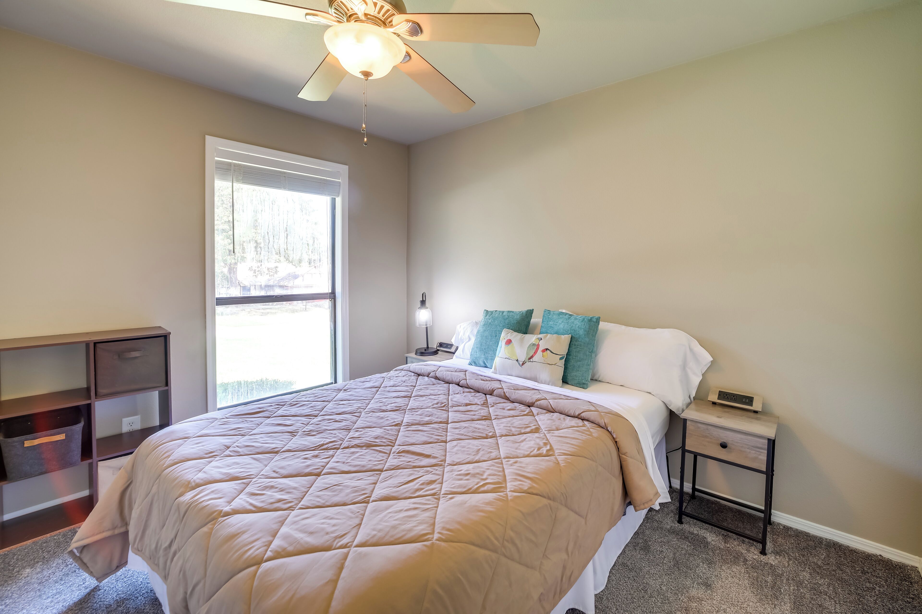 A bedroom with a bed, a nightstand, a ceiling fan, a window, and a desk.