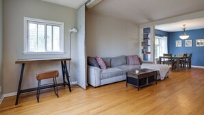 A spacious living room with a wooden floor, a grey sofa, a coffee table, and a dining area with a table and chairs.
