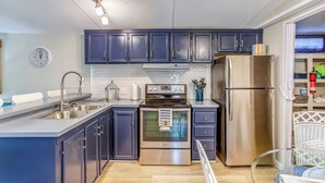 Une cuisine moderne avec des meubles de couleur bleu foncé, des appareils en acier inoxydable, un pare-feu blanc en carreaux et une horloge au mur.