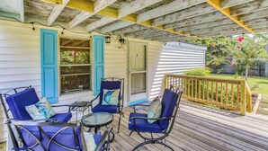 Une terrasse couverte avec des chaises bleues et une petite table, des rampes en bois et une vue sur un jardin.