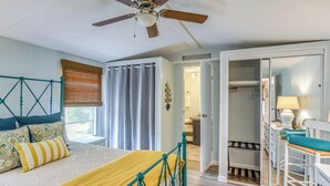 Une chambre à coucher comprenant un lit, un ventilateur de plafond, une fenêtre avec des rideaux, une armoire et un bureau avec une lampe.