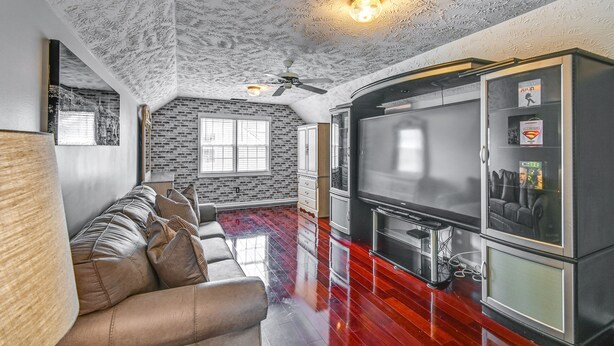 A living room with a brick wall, a sofa, a flat-screen TV, and a ceiling fan. - Roomy Fayetteville Home Rental w/ Screened Porch! (Fayetteville)