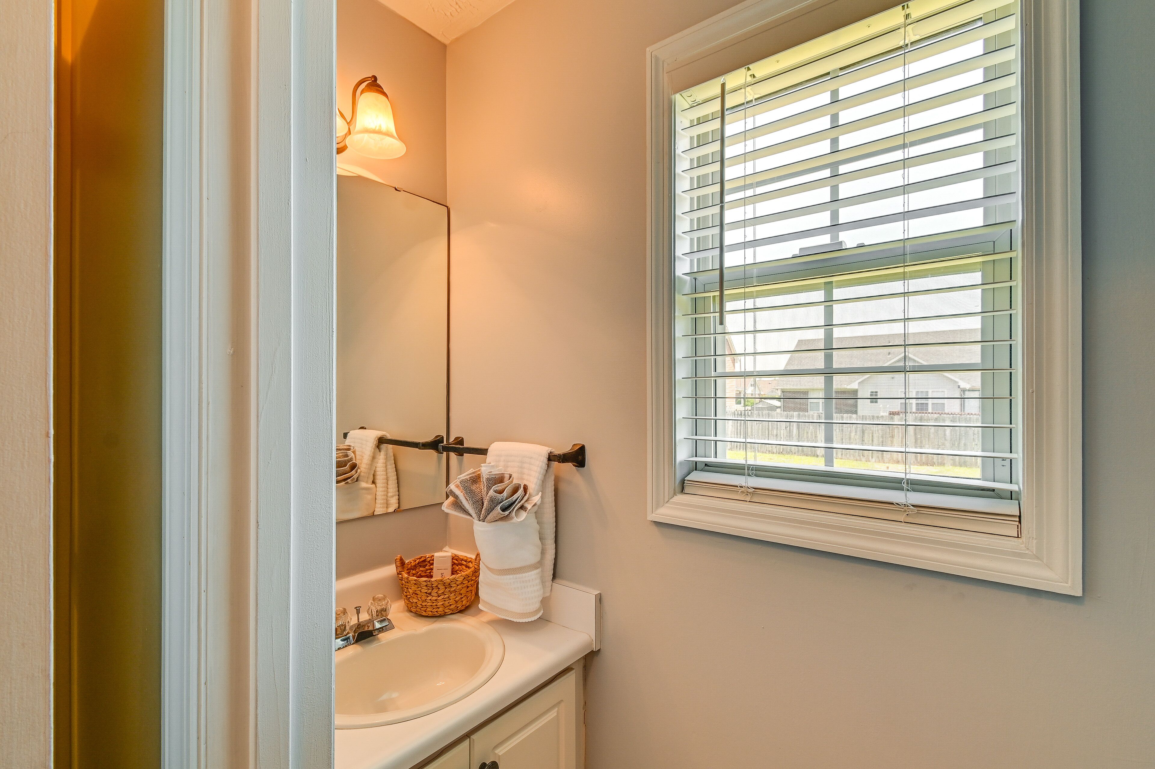 A bathroom with a sink, mirror, towel rack, and window with blinds.