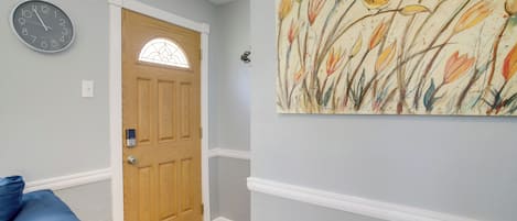 A hallway with a wooden door, a clock, and a wall-mounted artwork.