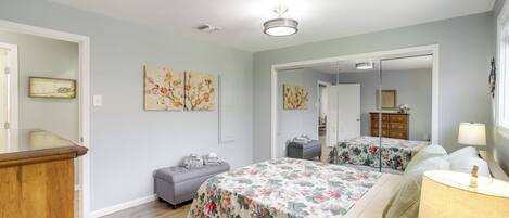 Ein Schlafzimmer mit zwei Betten, einer Holzkommode, einer grauen Bank und floralen Bildern an den Wänden.