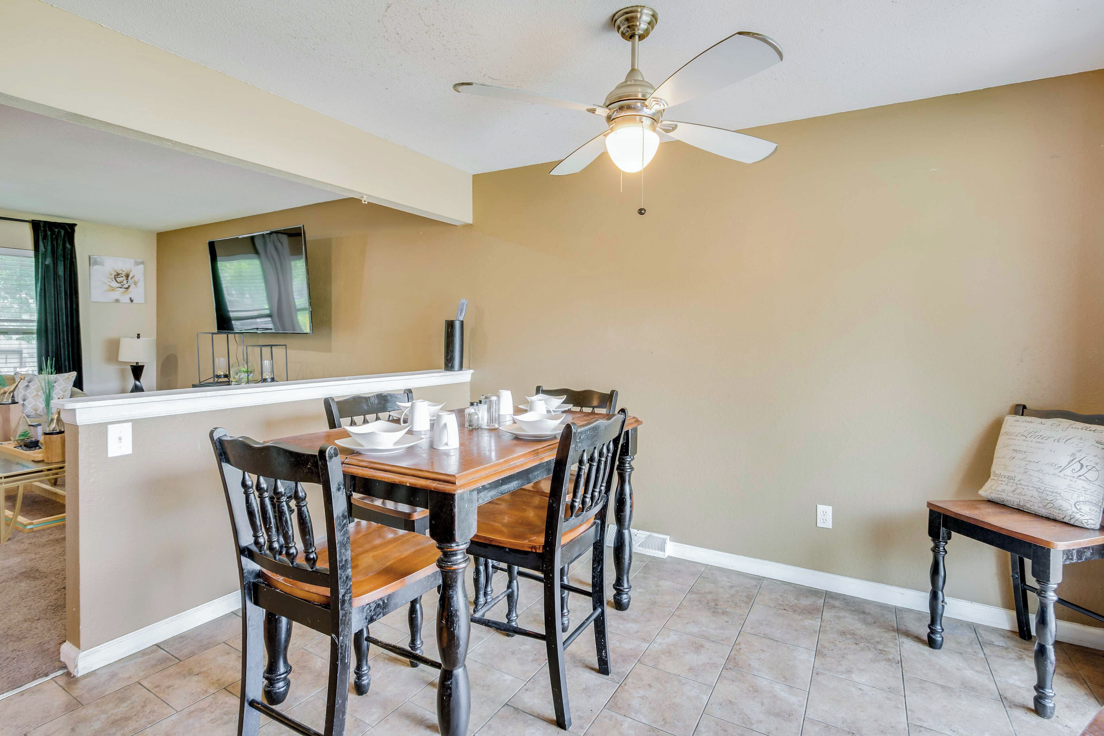 A dining area with a wooden table and chairs, a ceiling fan, and a television mounted on the wall.