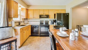A kitchen with wooden cabinets, a microwave, a refrigerator, and a dining table set with plates and cups. - Cozy Missouri Retreat w/ Deck & Grill, Near Hiking (Lee's Summit)