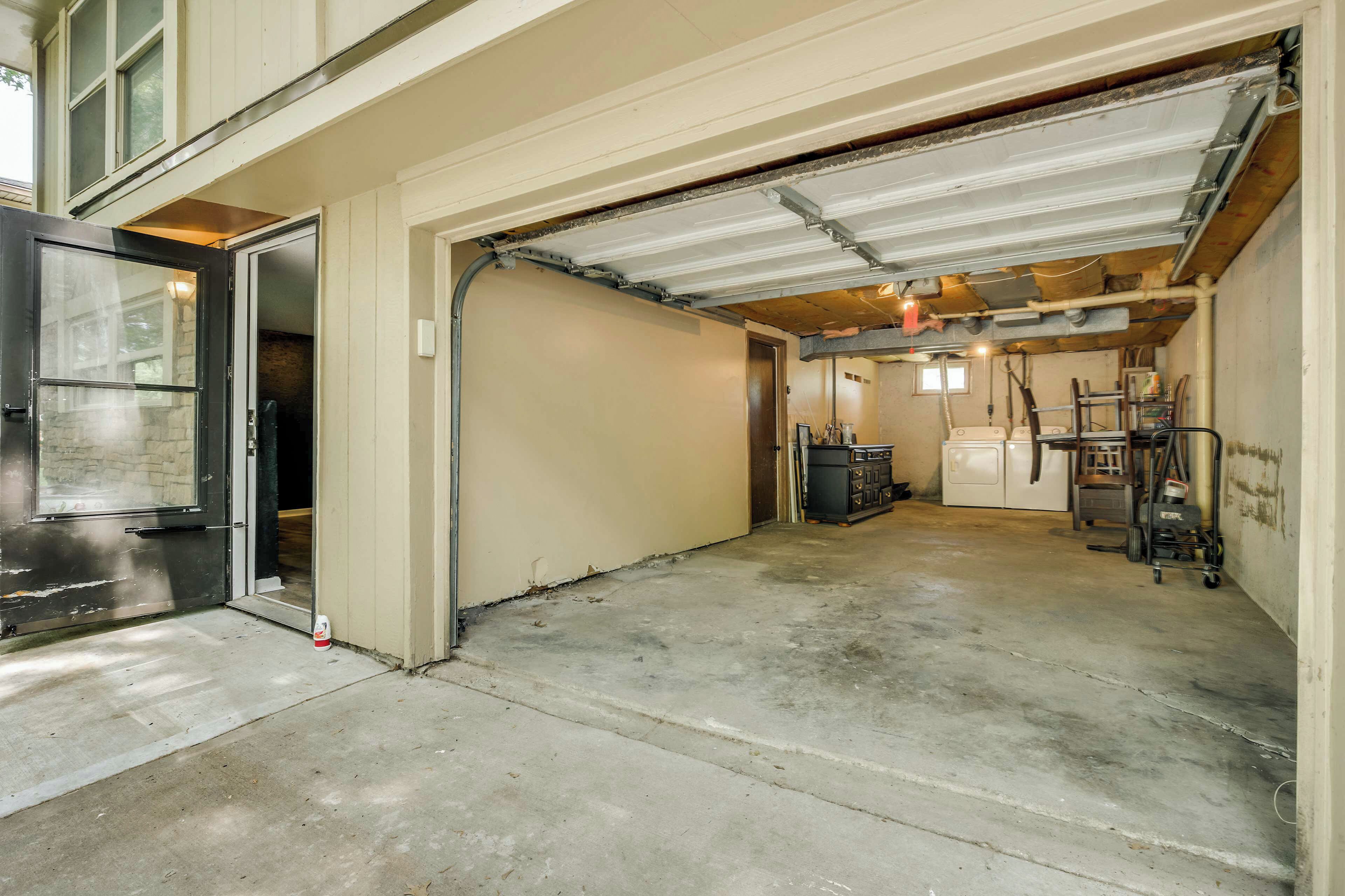 A garage with a concrete floor, a door leading to a vehicle, and a utility area with equipment.