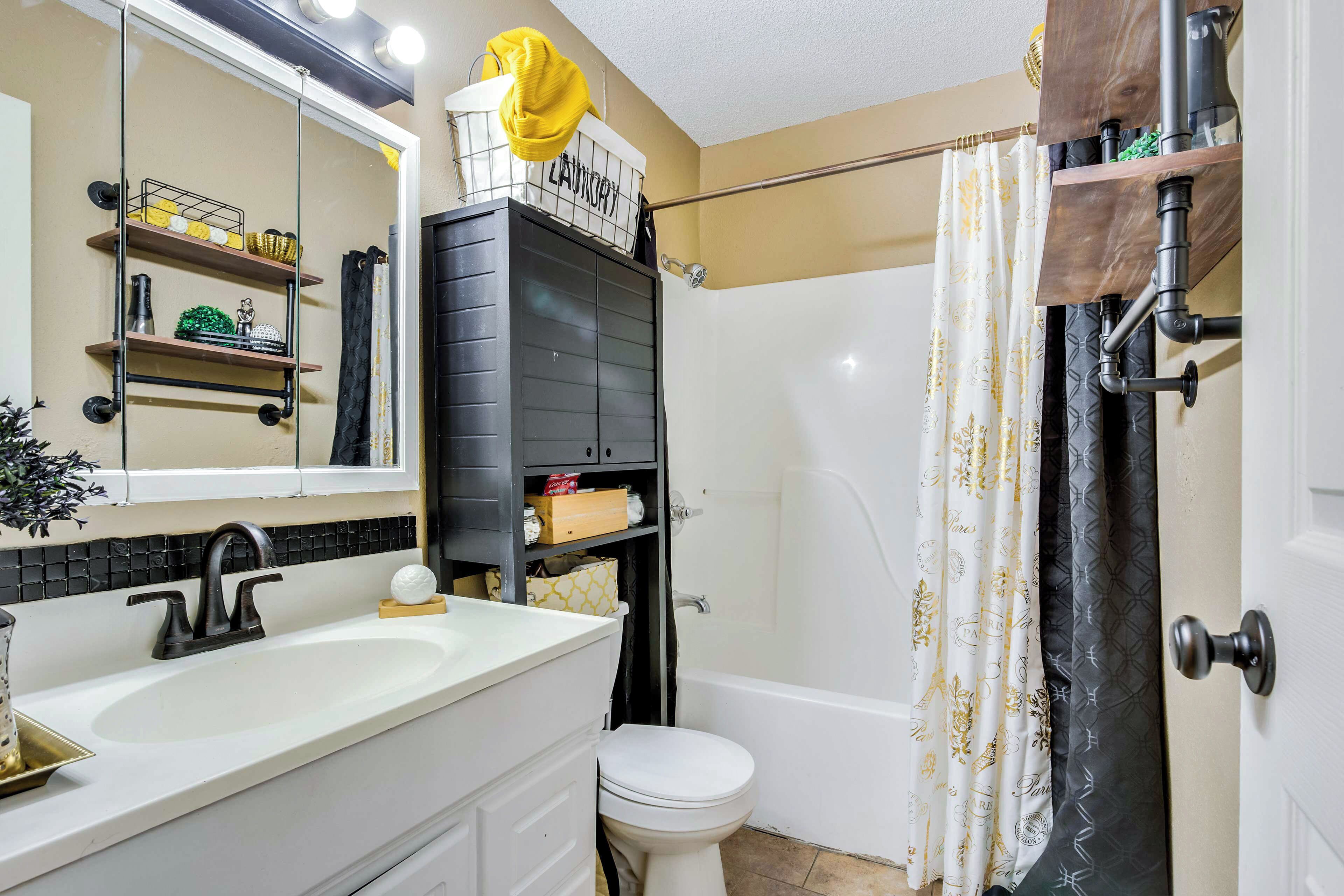 Un baño con un lavamanos blanco, estantes negros, un inodoro blanco y una cortina de ducha con un estampado.