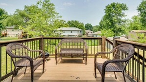 A wooden deck with wicker chairs and a table, overlooking a residential area with houses and trees. - Cozy Missouri Retreat w/ Deck & Grill, Near Hiking (Lee's Summit)