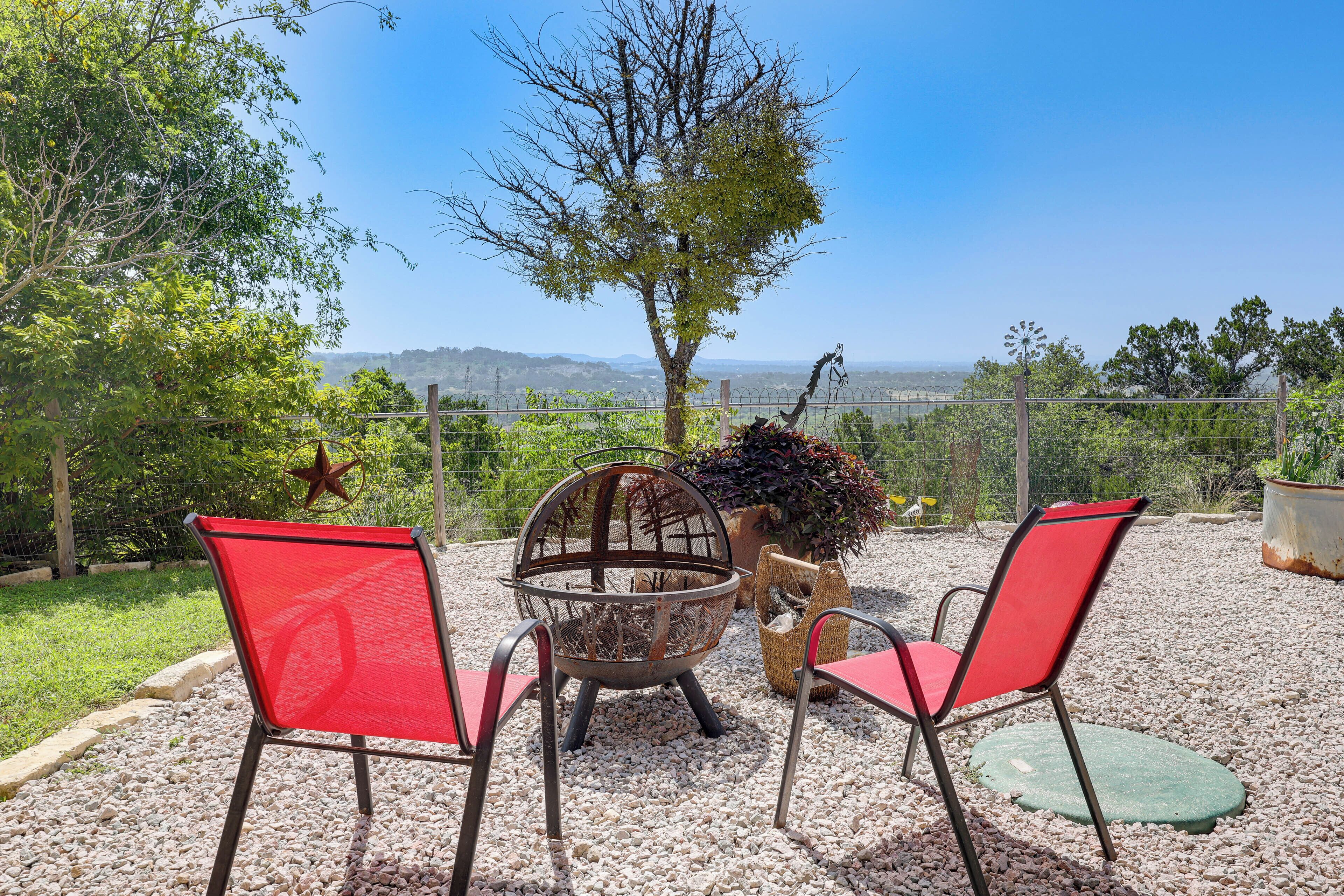 Un espace extérieur aménagé avec deux chaises rouges et une table en métal, entouré de gravier, et offrant une vue sur des collines lointaines.