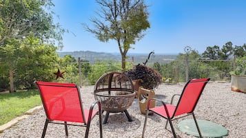 Un espace extérieur aménagé avec deux chaises rouges et une table en métal, entouré de gravier, et offrant une vue sur des collines lointaines.