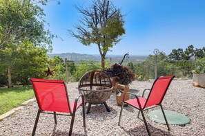 Un espacio al aire libre con dos sillas rojas y una mesa de metal, rodeado de grava, con vistas a colinas distantes.