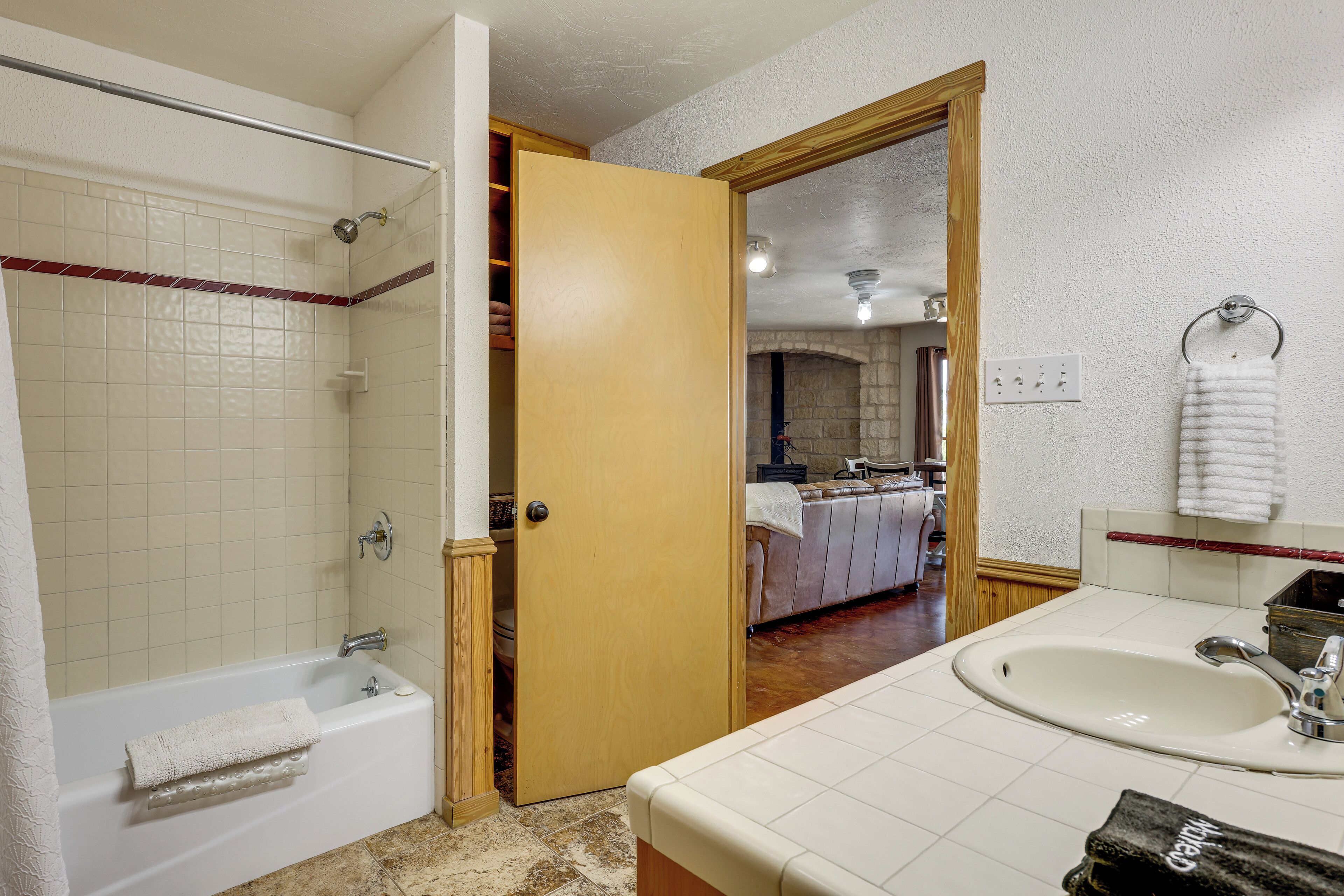 A bathroom with a bathtub, a shower, a sink, and a wooden door leading to a living area.