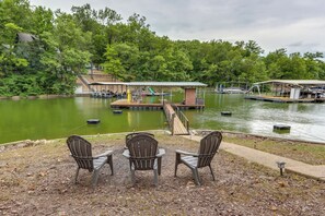 A lakeside deck with three Adirondack chairs, a wooden dock, and a covered seating area. - Dock + Screened Porch: Lake of the Ozarks Getaway! (Camdenton)