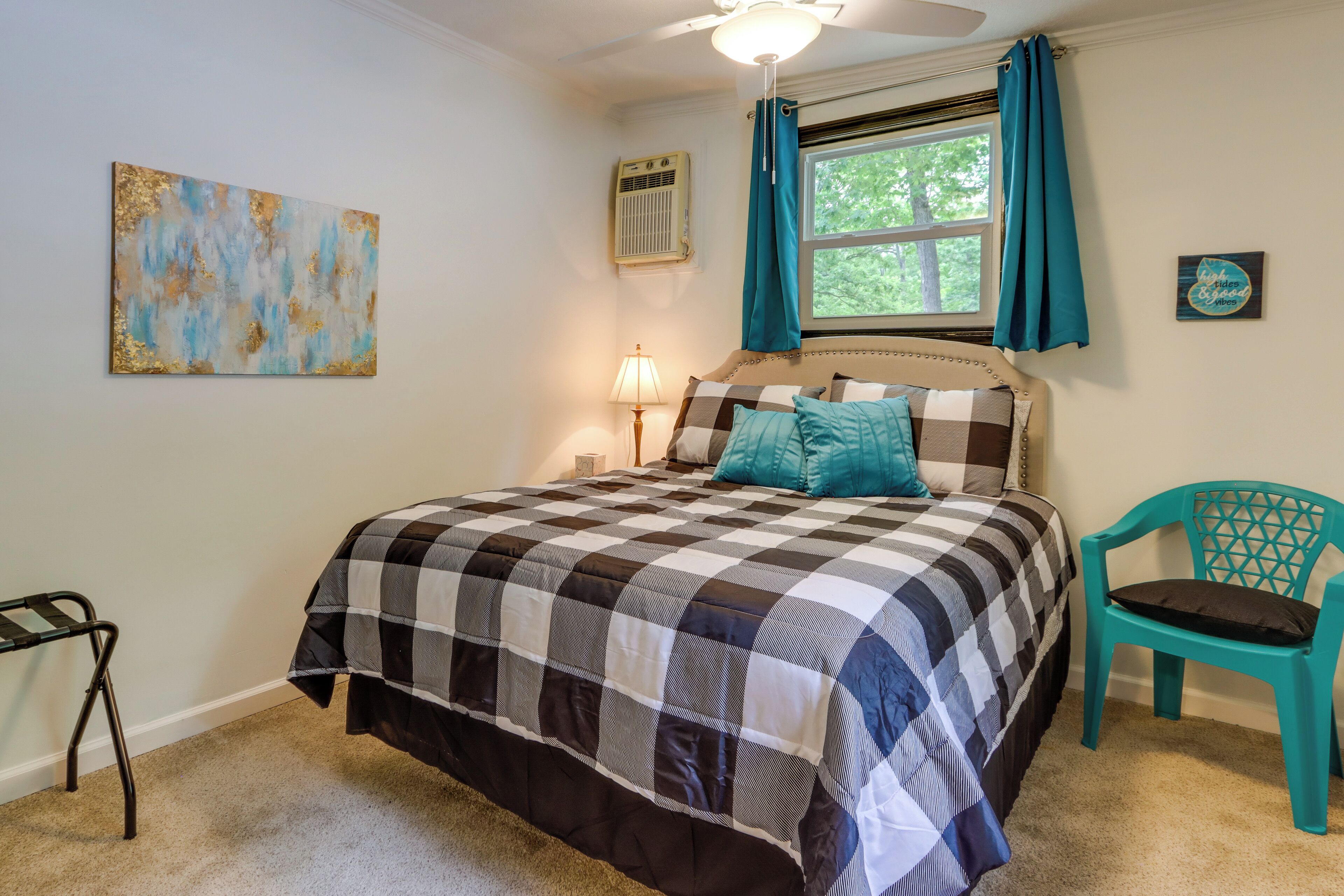 A bedroom with a checkered bedspread, a teal chair, a lamp, and a painting on the wall.