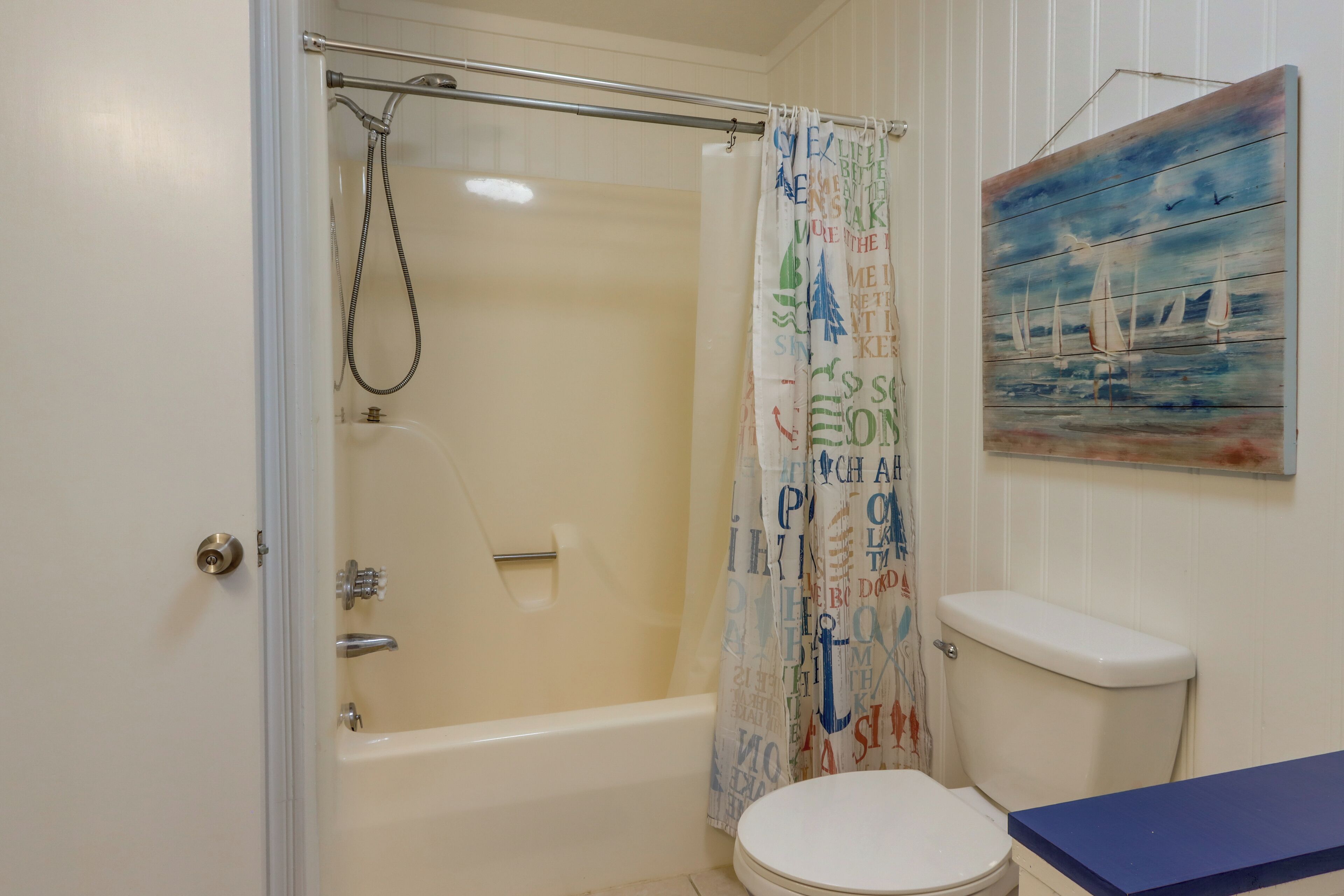Un baño con bañera, inodoro y cortina de ducha con motivos náuticos.