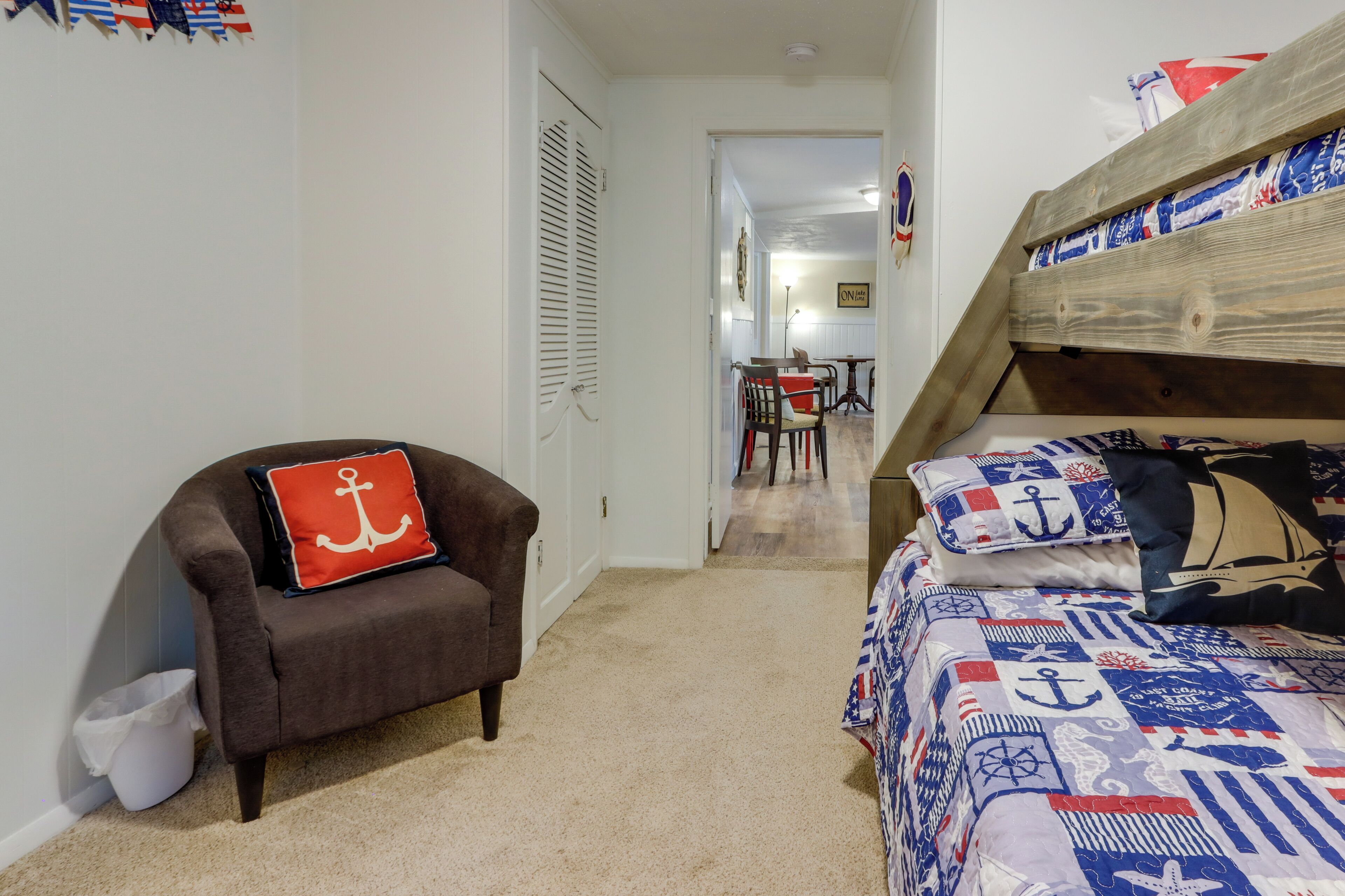 A bedroom with a bunk bed, a chair with a red pillow, and a carpeted floor.