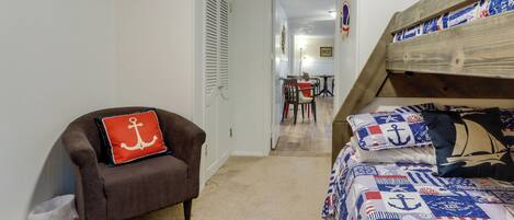 Un dormitorio con una cama litera, una silla con un cojín rojo y piso alfombrado.