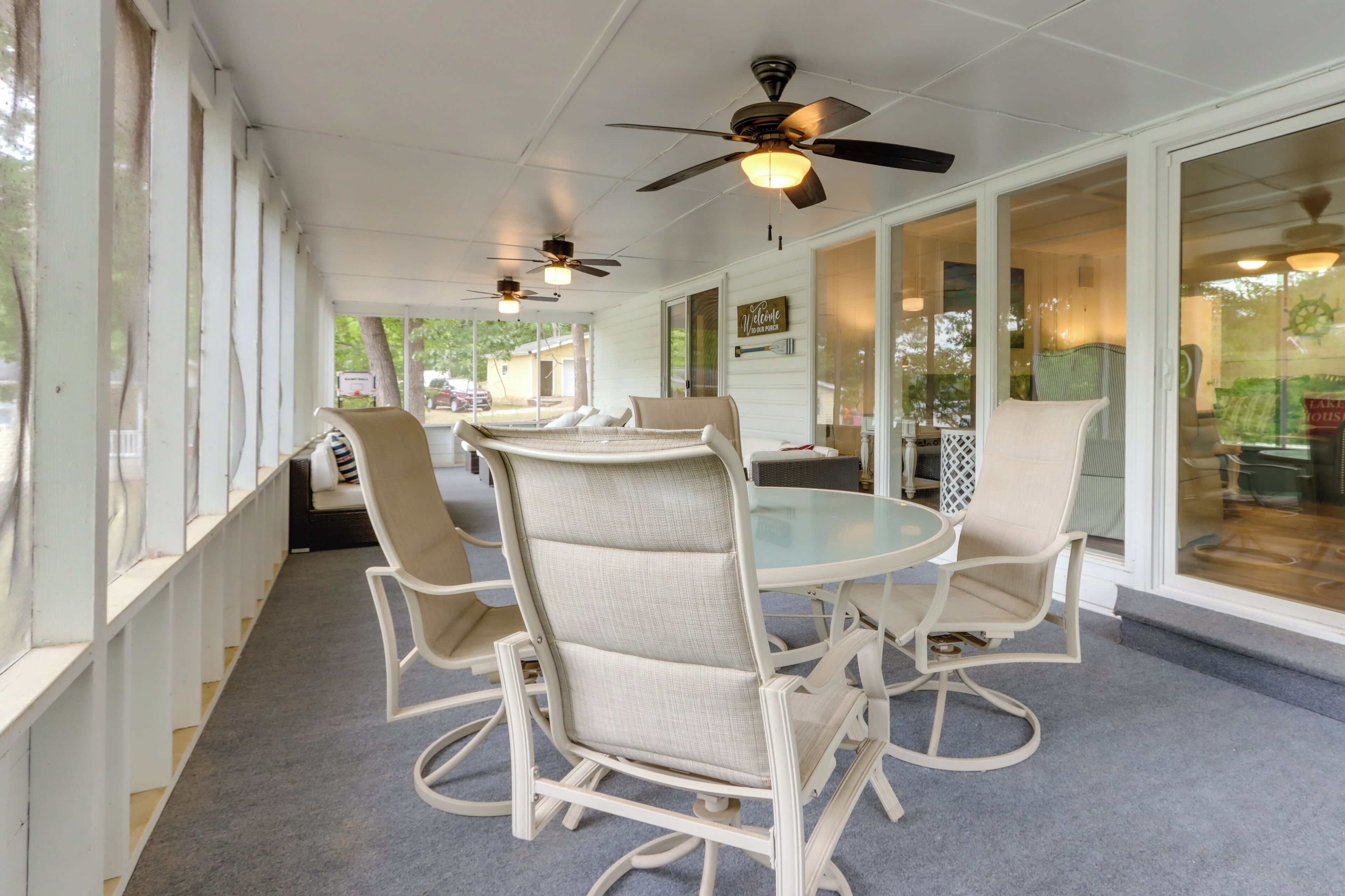 Une terrasse couverte avec une table ronde et quatre chaises, des ventilateurs de plafond et de grandes fenêtres.